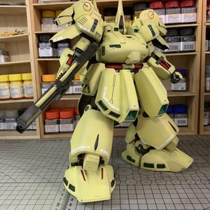 May include: A light yellow model robot with a large gun, red accents, and green details. The model is standing on a grid surface. The text "ArrowModelBuild" is visible in the image.