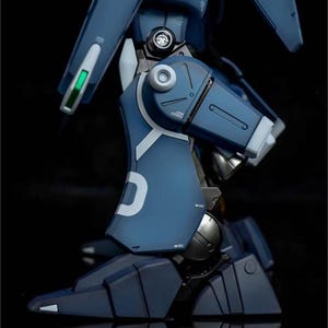 May include: A detailed view of a blue and white model robot leg. The leg features articulated joints, metallic accents, and a white "D" marking. The model is set against a dark background, highlighting its intricate design.