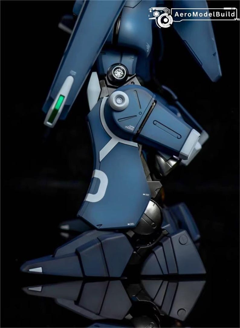 May include: A detailed view of a blue and white model robot leg. The leg features articulated joints, metallic accents, and a white "D" marking. The model is set against a dark background, highlighting its intricate design.