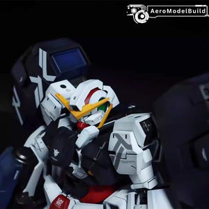 May include: A detailed model of a Gundam robot, featuring a white, black, and red color scheme. The model has intricate details, including a yellow face, green eyes, and various mechanical components. The AeroModelBuild logo is visible in the top right corner.