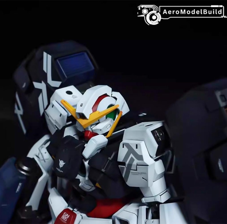 May include: A detailed model of a Gundam robot, featuring a white, black, and red color scheme. The model has intricate details, including a yellow face, green eyes, and various mechanical components. The AeroModelBuild logo is visible in the top right corner.