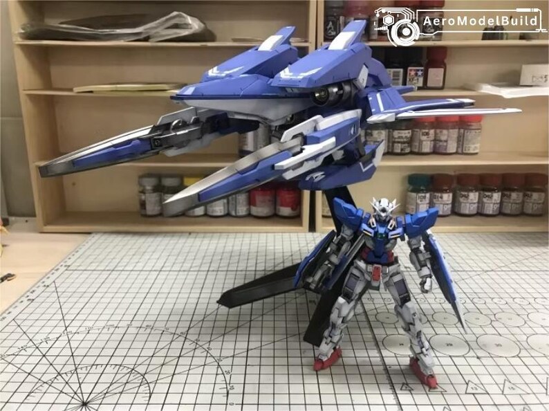 May include: A blue and white model of a futuristic aircraft with sharp, angular wings and a detailed robot figure. The robot is in a standing pose, with red and white accents. The model is on a grid-marked surface.