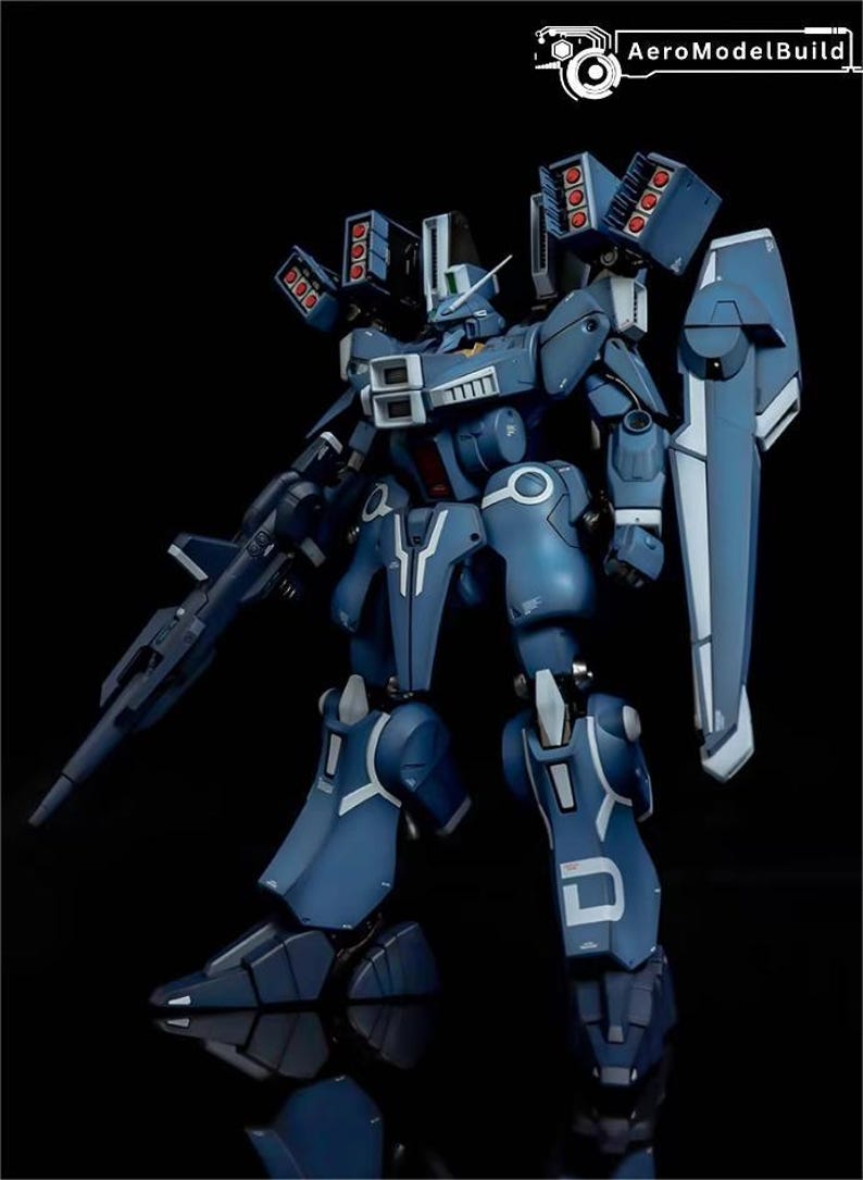 May include: A detailed model of a blue and white mecha robot with multiple missile launchers and a shield. The robot has intricate panel lines and is posed against a black background. The AeroModelBuild logo is in the top right corner.