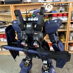 Pu&ograve; includere: Un modello dettagliato di robot blu scuro con una grande arma. Il robot presenta numerosi componenti meccanici, tra cui propulsori e uno scudo. Il logo AeroModelBuild &egrave; visibile in alto a destra.