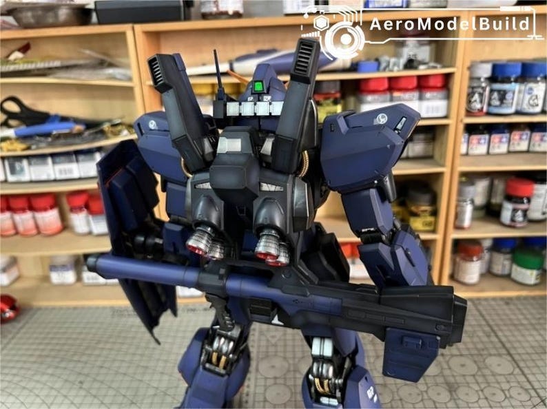 Pu&ograve; includere: Un modello dettagliato di robot blu scuro con una grande arma. Il robot presenta numerosi componenti meccanici, tra cui propulsori e uno scudo. Il logo AeroModelBuild &egrave; visibile in alto a destra.
