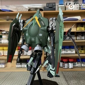 Puede incluir: Modelo detallado de un robot mec&aacute;nico verde y negro con grandes escudos y armas. El modelo est&aacute; sobre un soporte negro, con un dise&ntilde;o detallado. El fondo muestra estantes con botes de pintura y herramientas.