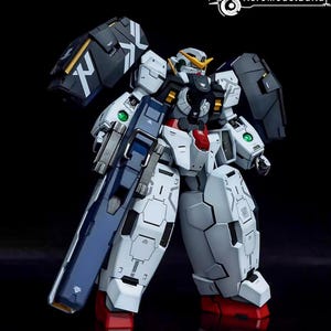 May include: A detailed model of a white, blue, and black robot with a large gun. The robot has articulated joints, angular armor plating, and red accents on its feet. The model has a futuristic design, with the AeroModelBuild logo in the top right corner.