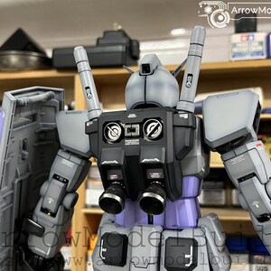 May include: A detailed model of a robot, primarily in shades of gray, black, and purple. The robot has a complex design with multiple components, including a shield, backpack, and various mechanical parts. The model is well-lit, showcasing its intricate details and craftsmanship.