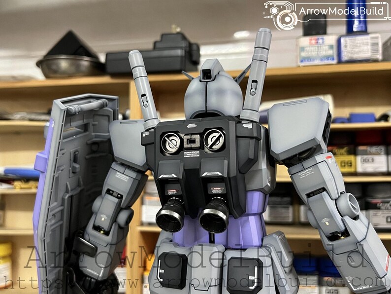 May include: A detailed model of a robot, primarily in shades of gray, black, and purple. The robot has a complex design with multiple components, including a shield, backpack, and various mechanical parts. The model is well-lit, showcasing its intricate details and craftsmanship.