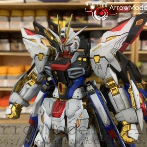 Puede incluir: Modelo detallado de un robot mecha, con una combinaci&oacute;n de colores blanco, azul, rojo y dorado. El robot tiene grandes alas y detalles intrincados en la armadura. El texto "ArrowModelBuild" es visible.