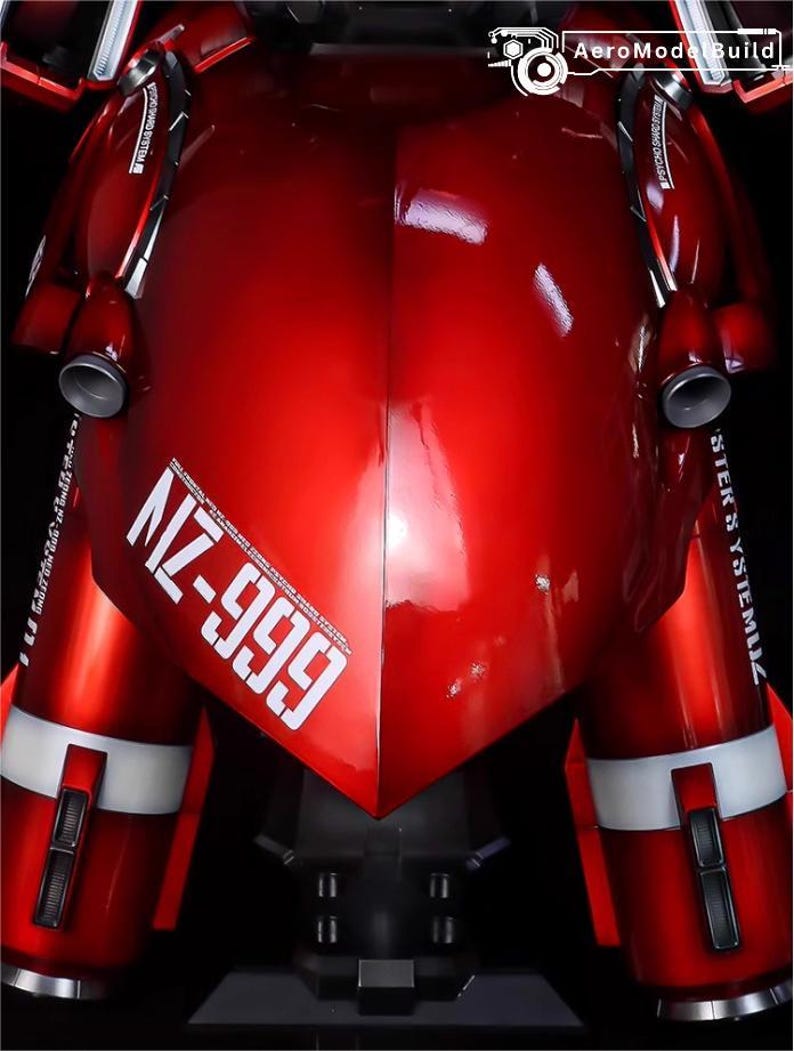 May include: A close-up of a red robot model with white accents and the text "NZ-999". The model has a glossy finish and features cylindrical components and metallic details. The AeroModeBuild logo is visible.