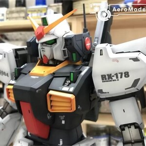 Op de afbeelding: Gedetailleerd model van een Gundam RX-178, met een wit, zwart, oranje en rood kleurenschema. Het model heeft ingewikkelde details, waaronder ventilatieopeningen, panelen en de tekst "RX-178" op de schouder. Het is een verzamelobject.
