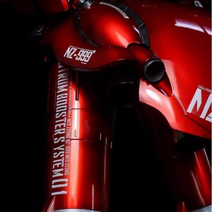 May include: A close-up of a red model robot with the text "NZ-999" and "TRUM BOOSTER SYSTEM 01". The model has a glossy finish and is set against a black background. The AeroModelBuild logo is in the top right corner.