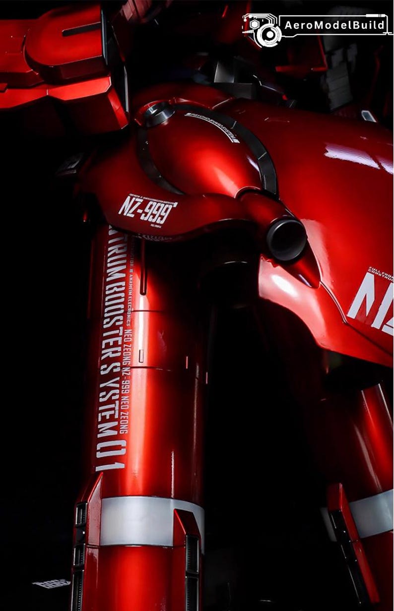 May include: A close-up of a red model robot with the text "NZ-999" and "TRUM BOOSTER SYSTEM 01". The model has a glossy finish and is set against a black background. The AeroModelBuild logo is in the top right corner.