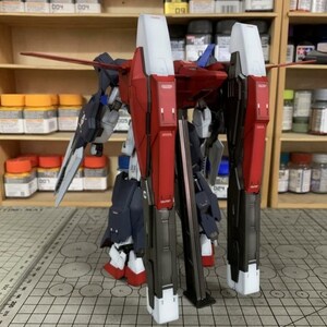 Puede incluir: Un kit de modelo de mecha parcialmente ensamblado, con componentes rojos, blancos y azul marino. El modelo tiene grandes piezas rectangulares para las piernas y alas. El kit est&aacute; sobre una esterilla de corte con un patr&oacute;n de cuadr&iacute;cula.