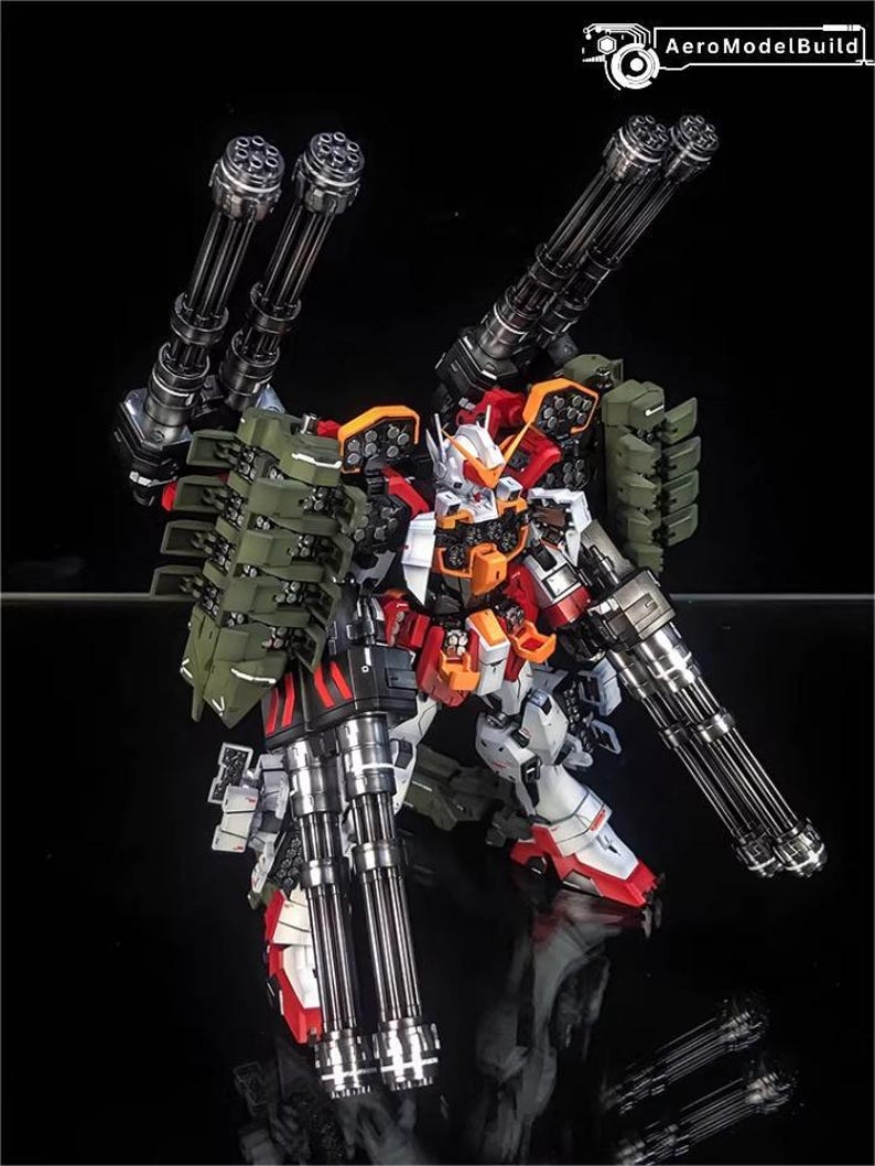 May include: A detailed model robot, predominantly white, red, and orange, with green detailing. It features multiple large, silver-coloured machine guns attached to its arms and back. The text "AeroModelBuild" is visible in the top right corner.