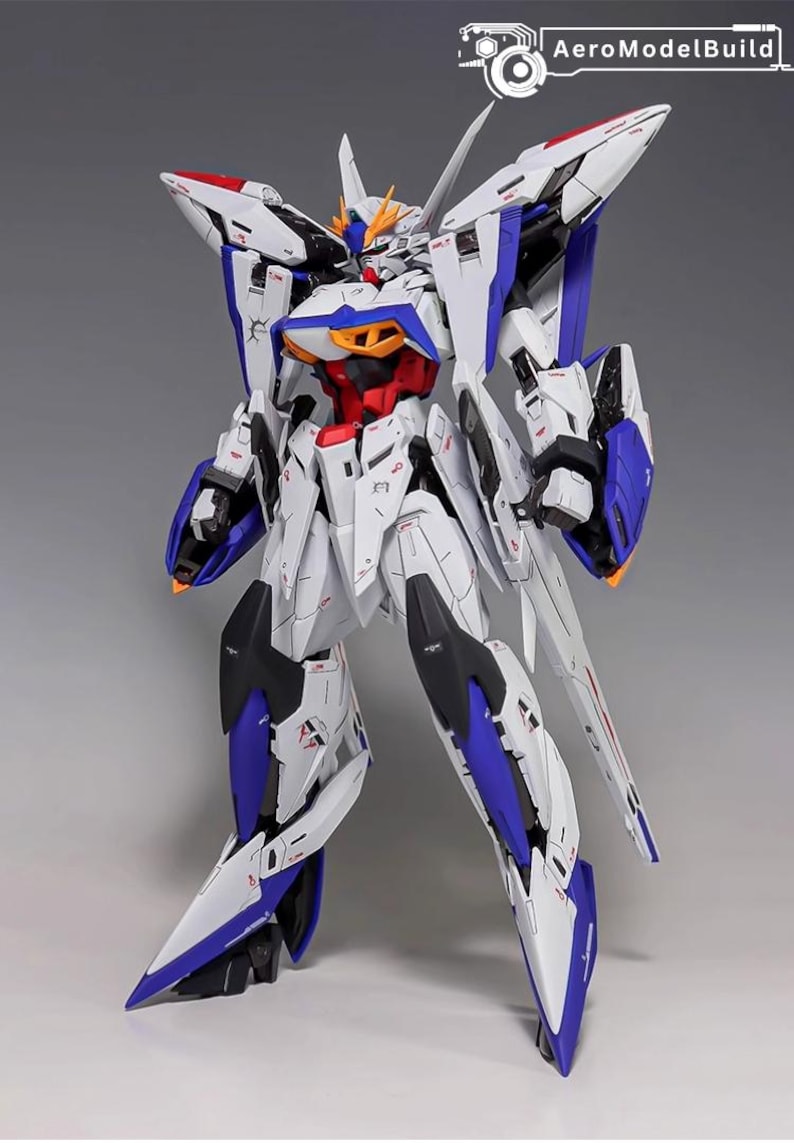 Puede incluir: Modelo detallado de un robot mecha blanco, azul, rojo y negro. El robot tiene un dise&ntilde;o complejo con &aacute;ngulos agudos y alas. El logotipo de AeroModelBuild es visible en la esquina superior derecha.