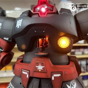 May include: A detailed model of a robot with a black and red color scheme. The robot has a glowing red light on top and a yellow light on the front. The model has intricate details and markings, including the text "A12" and "MS-06S".