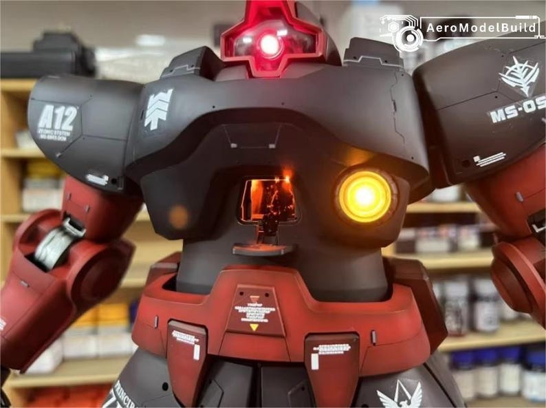 May include: A detailed model of a robot with a black and red color scheme. The robot has a glowing red light on top and a yellow light on the front. The model has intricate details and markings, including the text "A12" and "MS-06S".