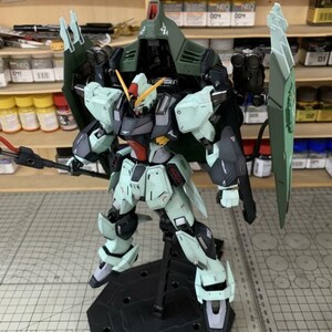 Puede incluir: Modelo detallado de un robot Gundam, con una combinaci&oacute;n de colores verde claro, negro y gris. El modelo est&aacute; posado sobre un soporte negro, mostrando su intrincado dise&ntilde;o y armamento. El robot tiene un gran escudo y un arma similar a una lanza.