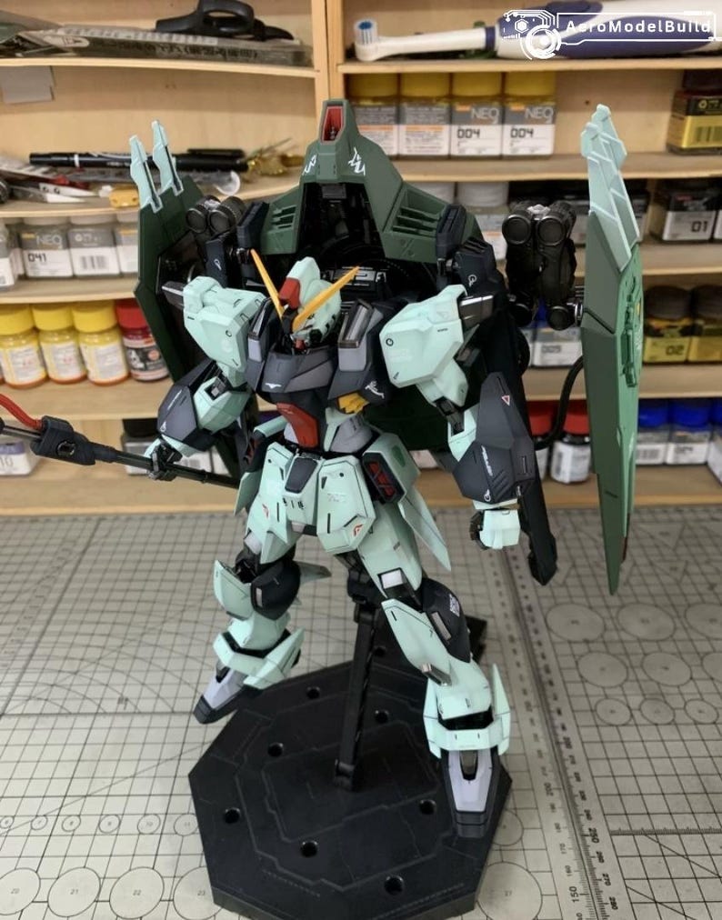 Puede incluir: Modelo detallado de un robot Gundam, con una combinaci&oacute;n de colores verde claro, negro y gris. El modelo est&aacute; posado sobre un soporte negro, mostrando su intrincado dise&ntilde;o y armamento. El robot tiene un gran escudo y un arma similar a una lanza.
