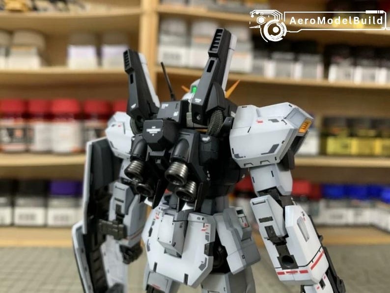 Pode incluir: Kit de modelo detalhado de um rob&ocirc; mecha, principalmente branco e preto, com detalhes mec&acirc;nicos intrincados. O rob&ocirc; tem grandes componentes montados nos ombros e m&uacute;ltiplos propulsores. O logotipo AeroModelBuild &eacute; vis&iacute;vel.