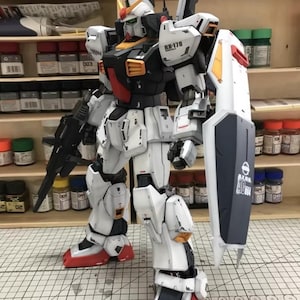 Op de afbeelding: Gedetailleerd model van een witte, zwarte en rode robot met een schild en een geweer. De robot heeft ingewikkelde mechanische details en staat op een rasteroppervlak. Een verzamelobject.