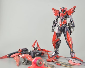 May include: A detailed model kit of a red, black, and silver robot with multiple components. The robot is standing upright, with various detached parts and weapons scattered around it. The model features intricate designs and sharp angles.