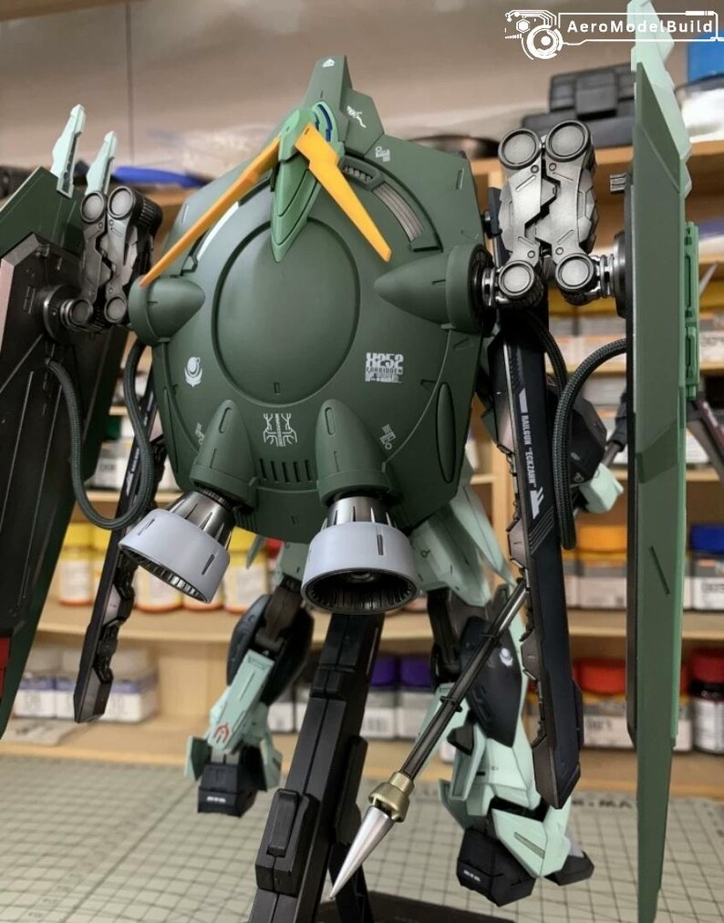 Puede incluir: Modelo detallado de un robot mec&aacute;nico verde y blanco con varios accesorios, incluyendo un escudo, una lanza y m&uacute;ltiples propulsores. El modelo tiene detalles intrincados y est&aacute; montado sobre un soporte negro. El logotipo de AeroModelBuild es visible en la esquina superior derecha.
