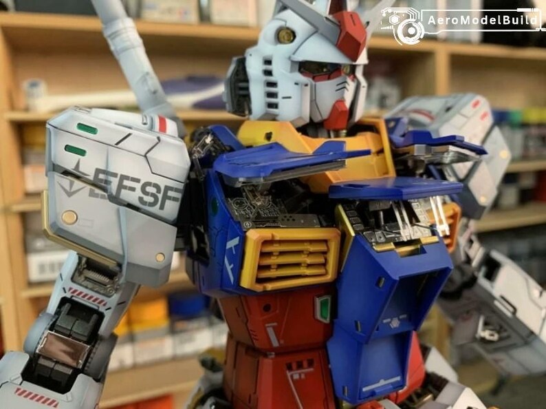 K&ouml;nnte beinhalten: Detailliertes Modell eines Gundam-Roboters mit wei&szlig;em Kopf, roten und gelben Akzenten, blauem und gelbem Torso und roten Beinen. Das Modell weist komplizierte mechanische Details auf, und der Text "EFSF" ist auf der Schulter sichtbar.