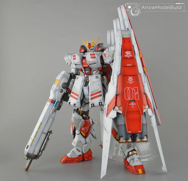 May include: A detailed model of a white and red mecha robot with a large shield. The robot has intricate paneling, red accents, and the number "01" is visible. The model is standing on a clear stand against a grey background.