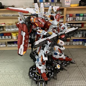 Puede incluir: Un detallado kit de modelo de un robot mecha, principalmente blanco y rojo, con intrincados detalles mec&aacute;nicos. El modelo est&aacute; montado sobre una plataforma en blanco y negro. La imagen incluye el texto "ArrowModelBuild" y "CUTTING MAT".