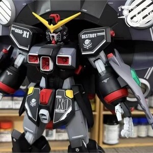 May include: A detailed model kit of a black, gray, and red robot with yellow accents. The robot has a large circular shield on its back and is labeled "GFAS-X1" and "DESTROY". The model is displayed in front of a shelf with various containers.