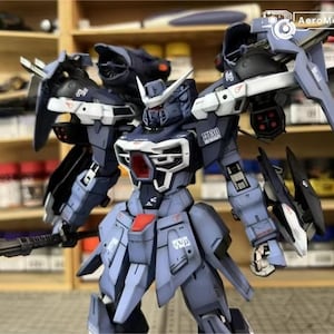 May include: A detailed model of a mecha robot, predominantly in shades of blue, gray, and white. The robot features intricate paneling, sharp edges, and various weapon attachments. The model is posed with a weapon in one hand, showcasing its complex design.
