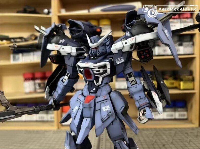 May include: A detailed model of a mecha robot, predominantly in shades of blue, gray, and white. The robot features intricate paneling, sharp edges, and various weapon attachments. The model is posed with a weapon in one hand, showcasing its complex design.