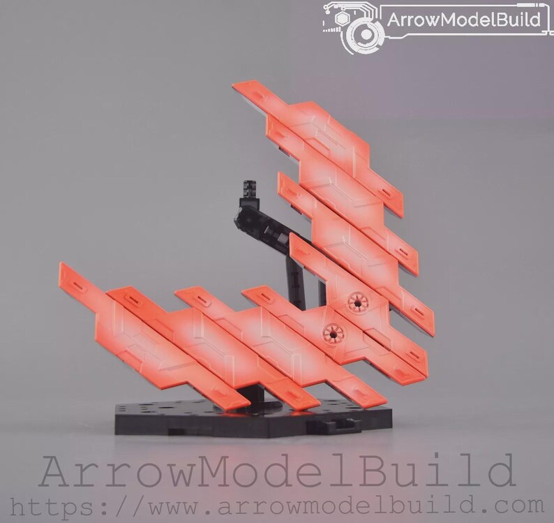 May include: A model kit component with orange and red angular panels, attached to a black stand and base. The panels have a gradient effect, transitioning from orange to red. The base is black, and the background is a solid grey.