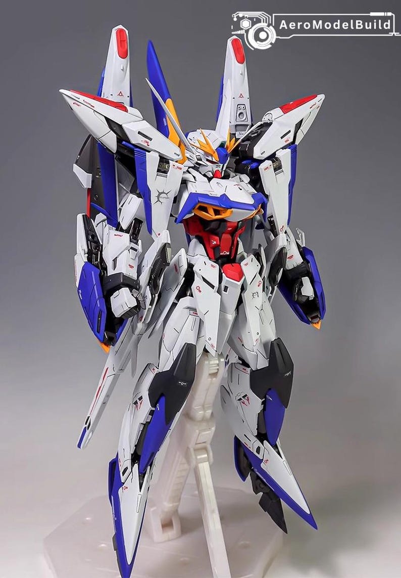 Puede incluir: Un modelo detallado de un robot futurista, principalmente blanco con acentos azules, rojos y amarillos. El robot tiene un dise&ntilde;o complejo con m&uacute;ltiples paneles, alas y una espada. El modelo est&aacute; sobre un soporte transparente.