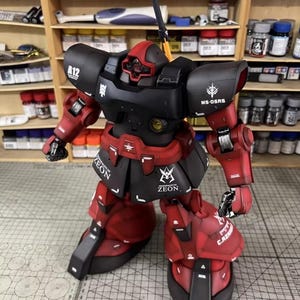 May include: A detailed model of a red and black robot with the text "ZEON" and "MS-OSRS". The robot has a red head and arms, with black armor and accents. The model is posed in a dynamic stance, showcasing its intricate design.
