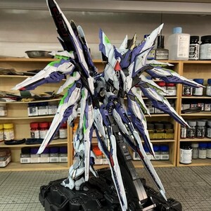 May include: A highly detailed model of a futuristic robot with large, stylized wings. The model features a complex design with white, blue, green, and red accents. It is mounted on a black base, showcasing intricate mechanical details.