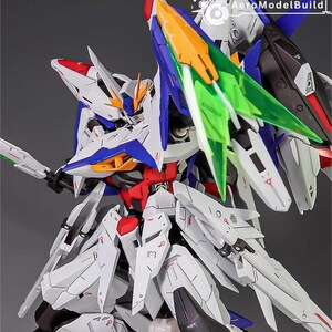 Puede incluir: Maqueta detallada de un robot futurista, principalmente blanco con detalles en azul, rojo y amarillo. El robot presenta paneles intrincados, bordes afilados y componentes transl&uacute;cidos verdes y naranjas. El logotipo de AeroModelBuild es visible.