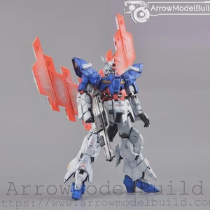 May include: A detailed model robot in white, blue, and red. It features large wings and a weapon. The image includes the text "ArrowModelBuild".