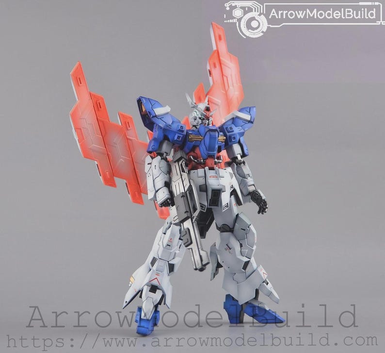 May include: A detailed model robot in white, blue, and red. It features large wings and a weapon. The image includes the text "ArrowModelBuild".