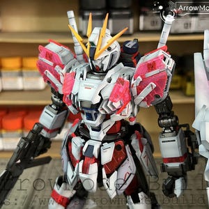 May include: A detailed model of a Gundam robot, primarily white, red, and pink. The robot has a complex design with multiple panels, weapons, and a shield. The model is posed in a dynamic stance, showcasing its intricate details.