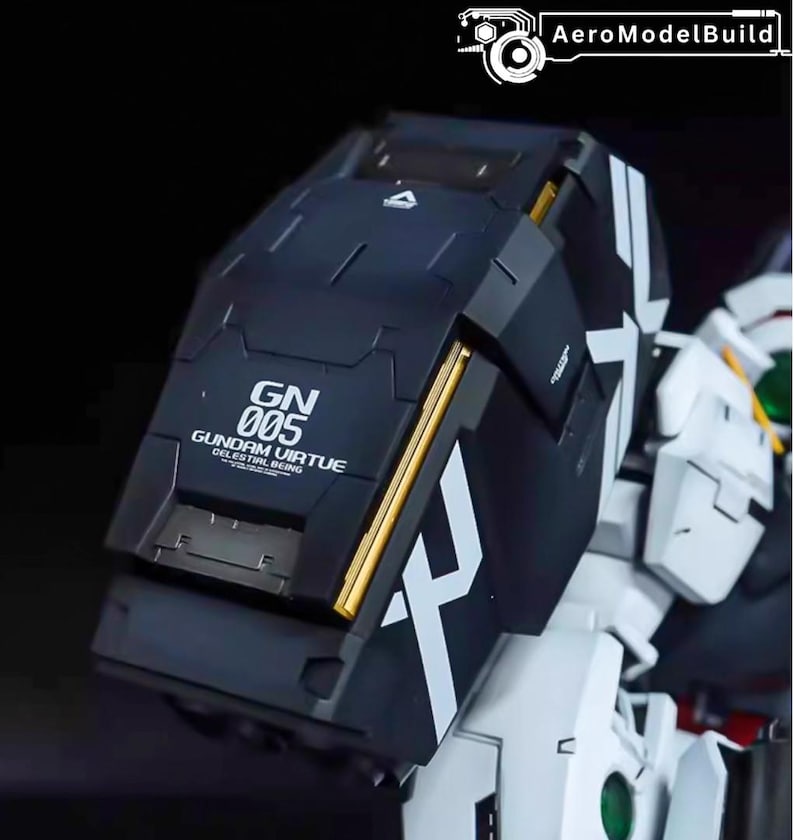 May include: A close-up of a black and white Gundam model kit. The model features a large, angular shield with gold accents and the text "GN 005 GUNDAM VIRTUE CELESTIAL BEING". The model is partially assembled.