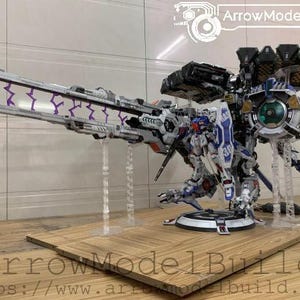 May include: A detailed model of a futuristic robot with a large cannon and multiple attachments. The robot is primarily white, blue, and gray, with purple lightning bolt accents. The model is displayed on a wooden base.