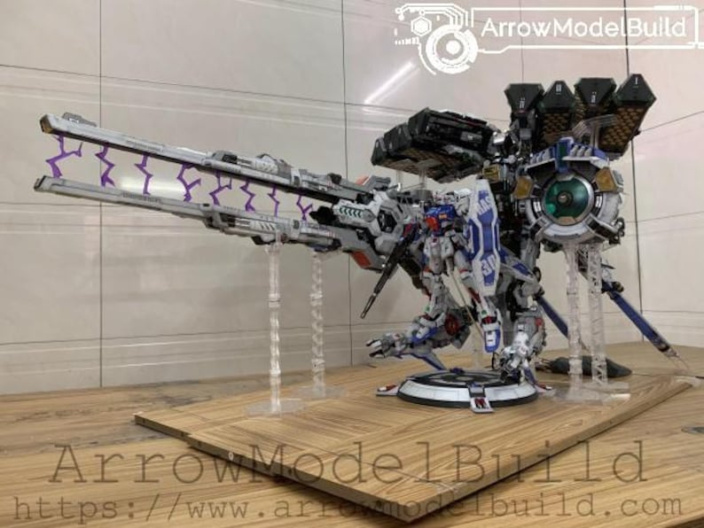 May include: A detailed model of a futuristic robot with a large cannon and multiple attachments. The robot is primarily white, blue, and gray, with purple lightning bolt accents. The model is displayed on a wooden base.