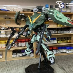 Puede incluir: Un modelo detallado de un robot mecha verde y blanco con grandes cuchillas y un escudo. El robot est&aacute; posado sobre un soporte negro, con un dise&ntilde;o detallado y m&uacute;ltiples partes articuladas. El fondo muestra estantes con suministros de pintura.