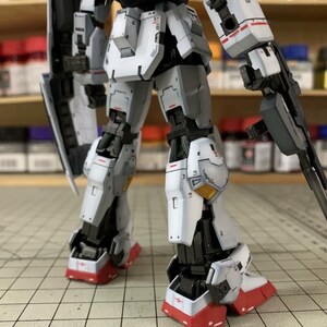 Pode incluir: Modelo de rob&ocirc; parcialmente montado, com esquema de cores branco, cinza, preto e vermelho. O rob&ocirc; tem uma arma e um escudo. O modelo est&aacute; em uma superf&iacute;cie quadriculada.