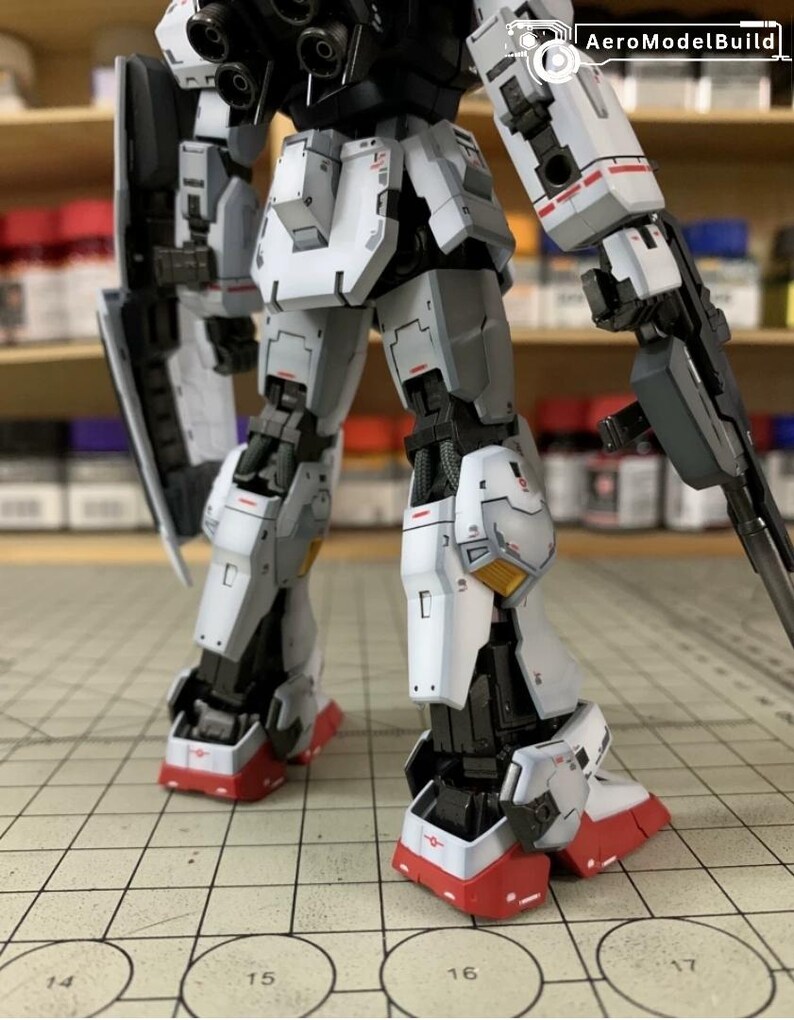 Pode incluir: Modelo de rob&ocirc; parcialmente montado, com esquema de cores branco, cinza, preto e vermelho. O rob&ocirc; tem uma arma e um escudo. O modelo est&aacute; em uma superf&iacute;cie quadriculada.