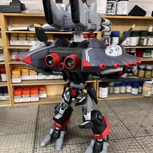 May include: A detailed model of a futuristic aircraft or robot, primarily in shades of gray, black, and red. The model features multiple jet engines, wings, and a complex mechanical design. The text "AeroModelBuild" is visible.